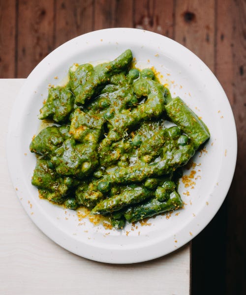 A plate of green gnocchi pasta with peas, on a white plate on top of a white table next to a wooden floor