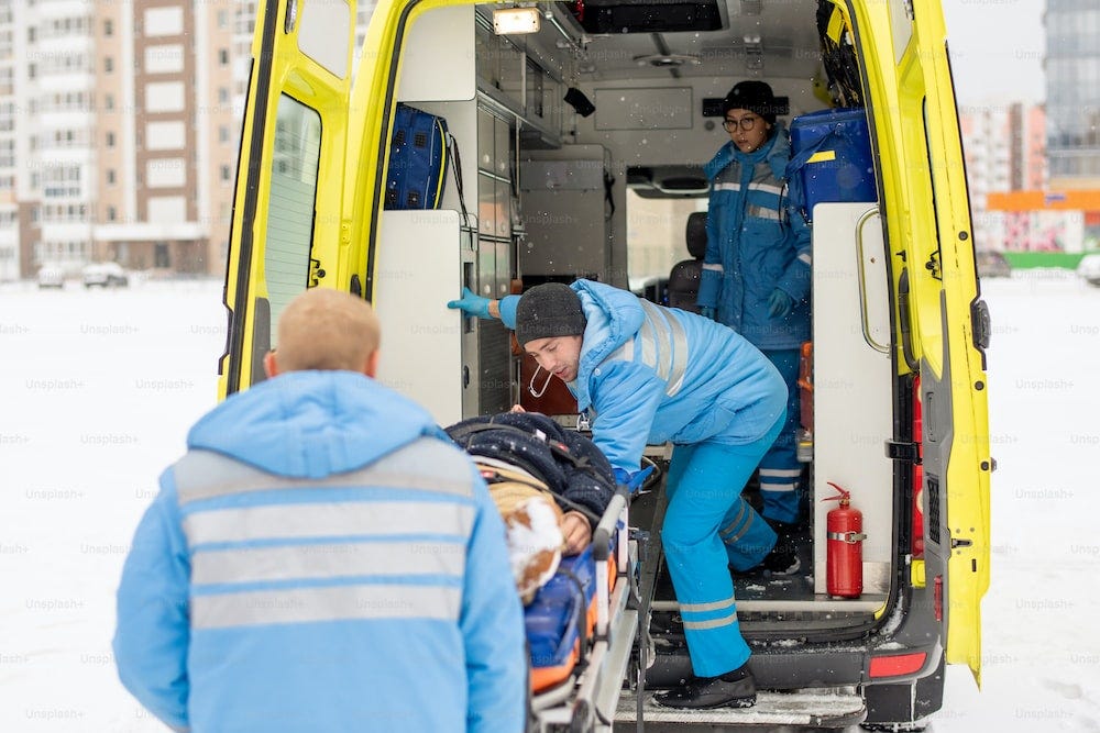 Paramedics in blue workwear getting stretcher with fixed unconscious man into ambulance car before going to hospital Paramedics in blue workwear getting stretcher with fixed unconscious man into ambulance car before going to hospital