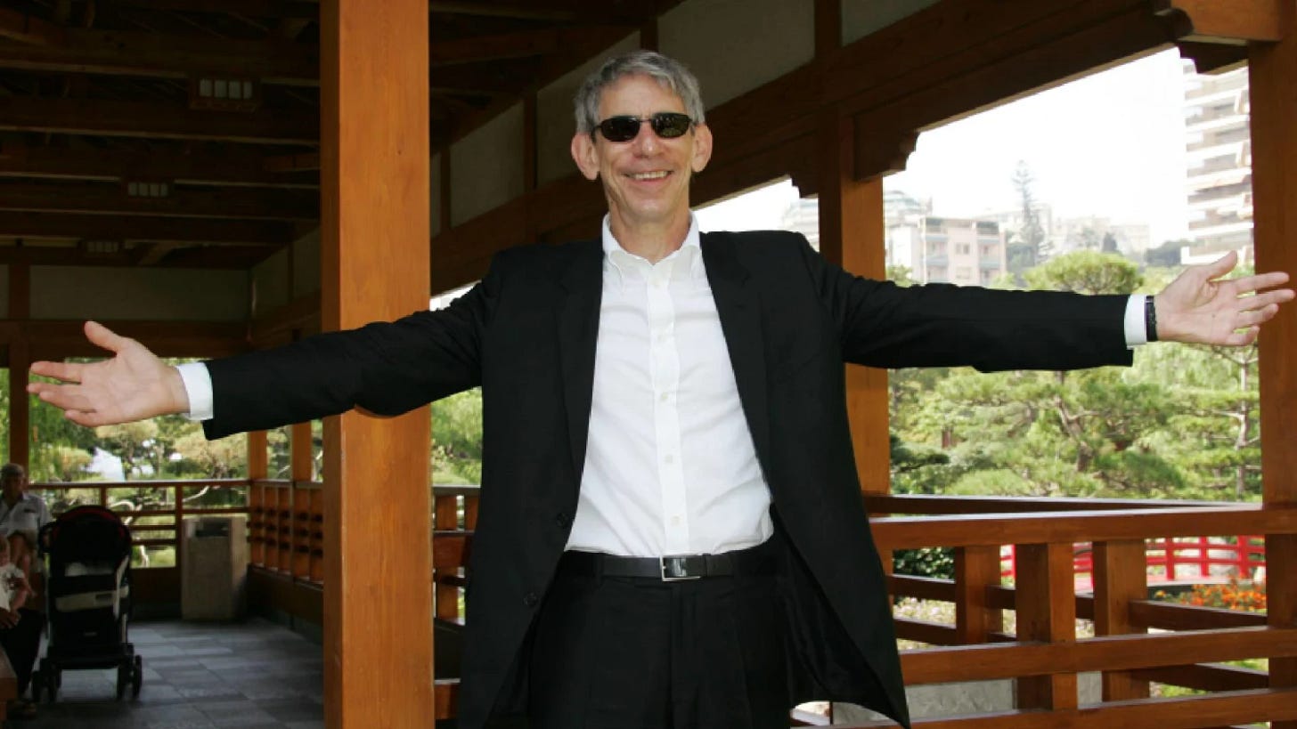 This photo shows actor, author, and comedian Richard Belzer (1944-2023) standing at the front entrance of an open-air bar with his arms stretched wide and a smile on his face. Belzer, best known for playing Detective John Munch for seven seasons on Paul Attanasio's Homicide: Life on the Street and for 15 seasons on Dick Wolf's Law and Order: Special Victims Unit, died at his home in Beaulieu-sur-Mer, France on 19 February 2023.