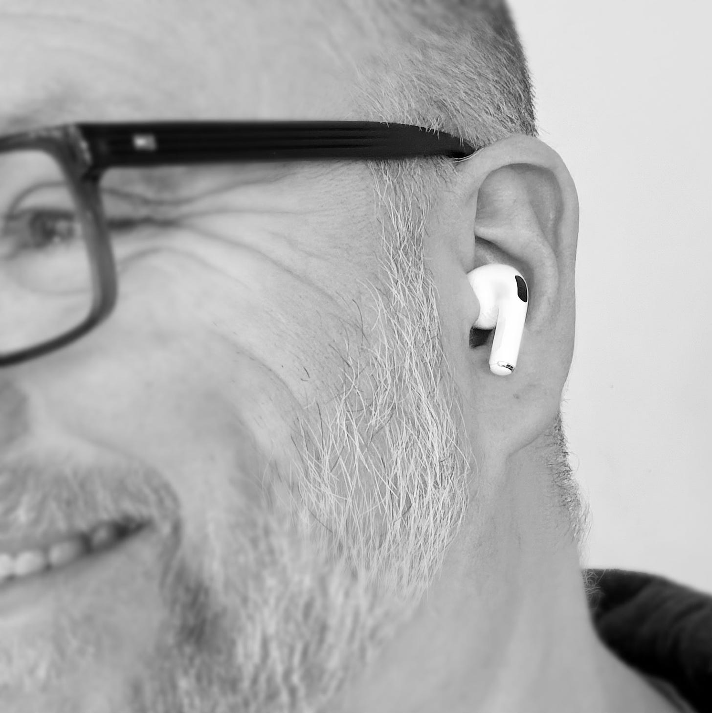 A black and white smiling photo of the authors face taken from the side with an emphasis placed in the white AirPods Pro