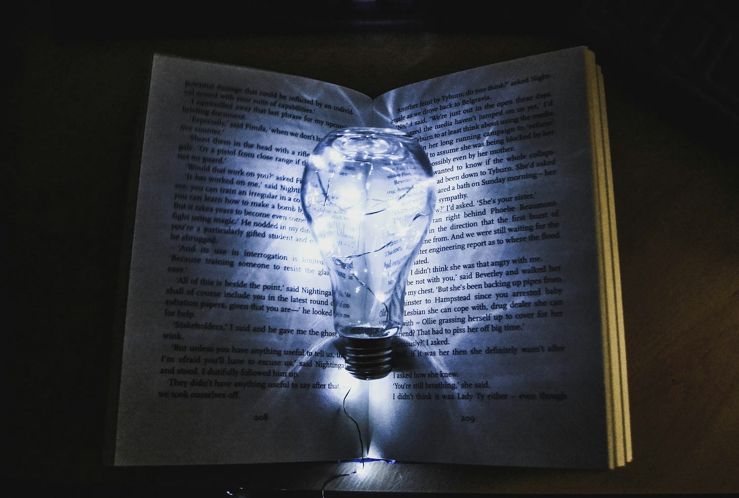 Sfondo nero con un libro aperto e in primo piano una lampadina che emana una luce azzurrina, illuminando le pagine centrali del libro.