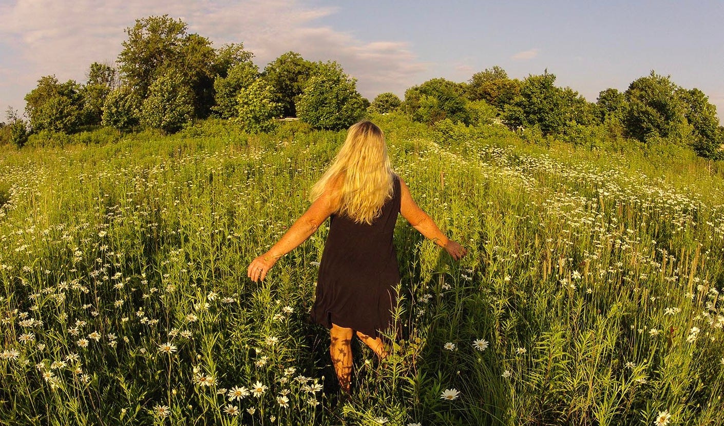 A girl in a field of daisies looking out at the sky.