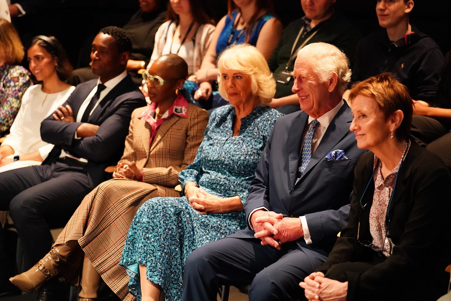 King Charles and Queen Camilla smiling and sitting in a theatre