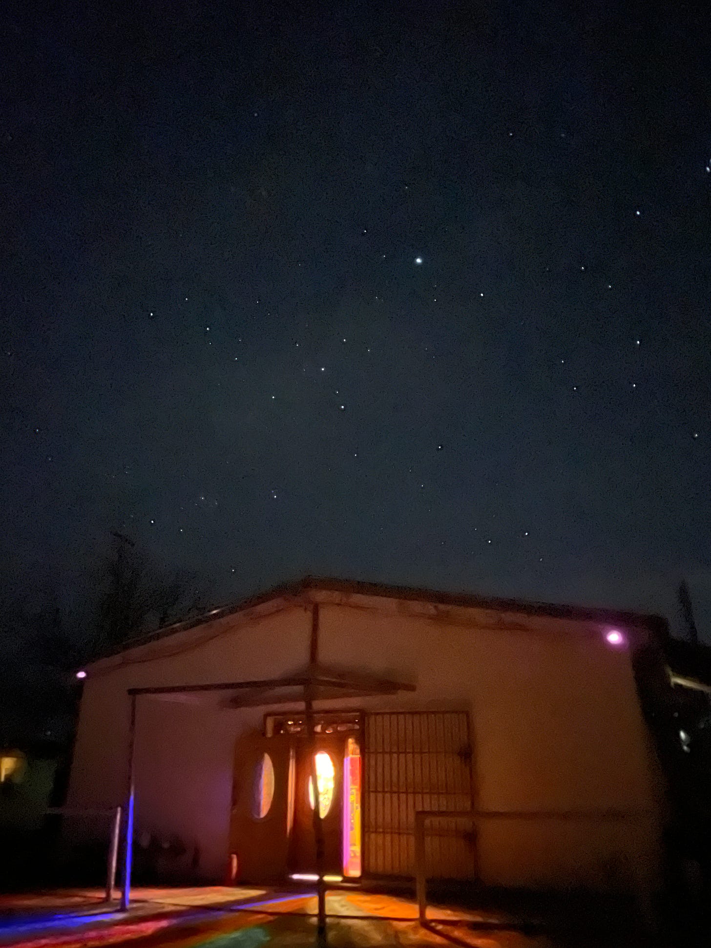 A studio building at Sonic Ranch under a starry night sky, with multicolor light emanating from its doorway