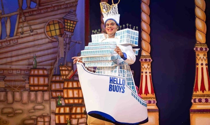 A panto dame in a cruise ship outfit with 'Hello buoys' on the side