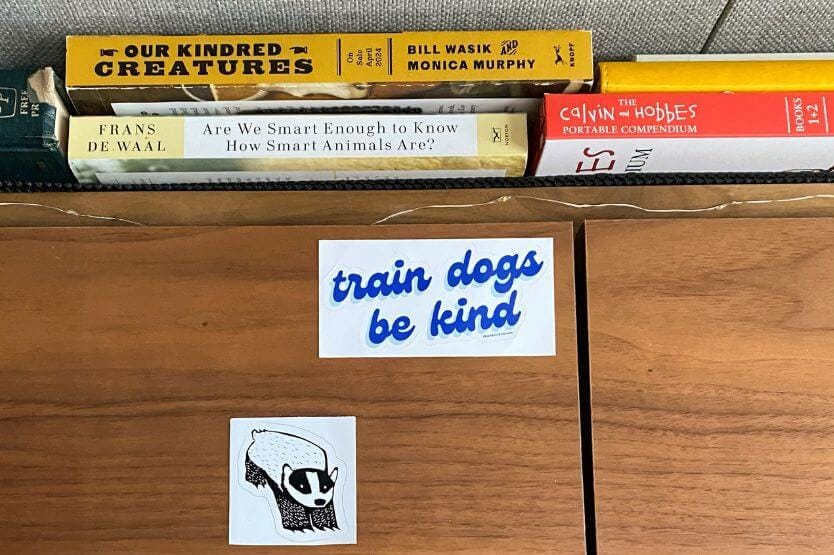 A close up of the sticker cabinet in our converted camper van that has a white sticker with blue text reading train dogs be kind