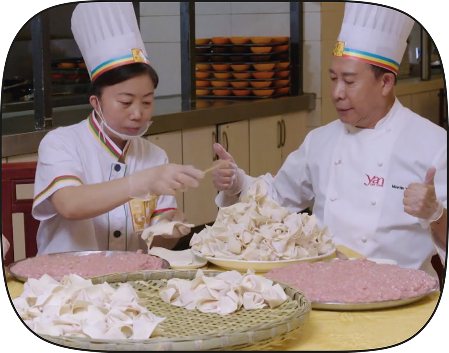 Chef Yan sits with Chef Yi behind a pile of chaoshou that they've just folded