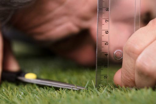Man cutting his grass with scissors and a ruler in a desperate act of perfectionism