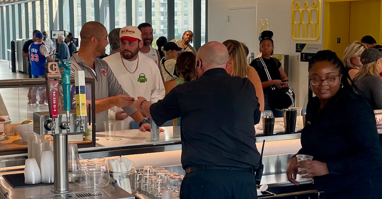 Bartenders fill drink orders while patrons stand three-deep in line.