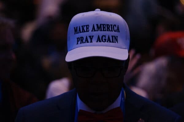Someone in a crowd wears a “Make America Pray Again” hat. 