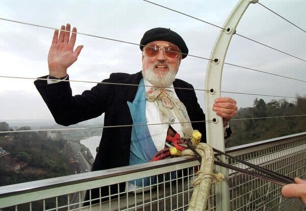 Mr. Kirke waving from the other side of a bridge while wearing a beret, sunglasses and a suit. Bungee cords are attached to his torso.