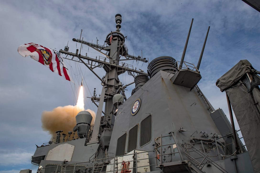 A missile launches into the sky behind the mast of a ship.