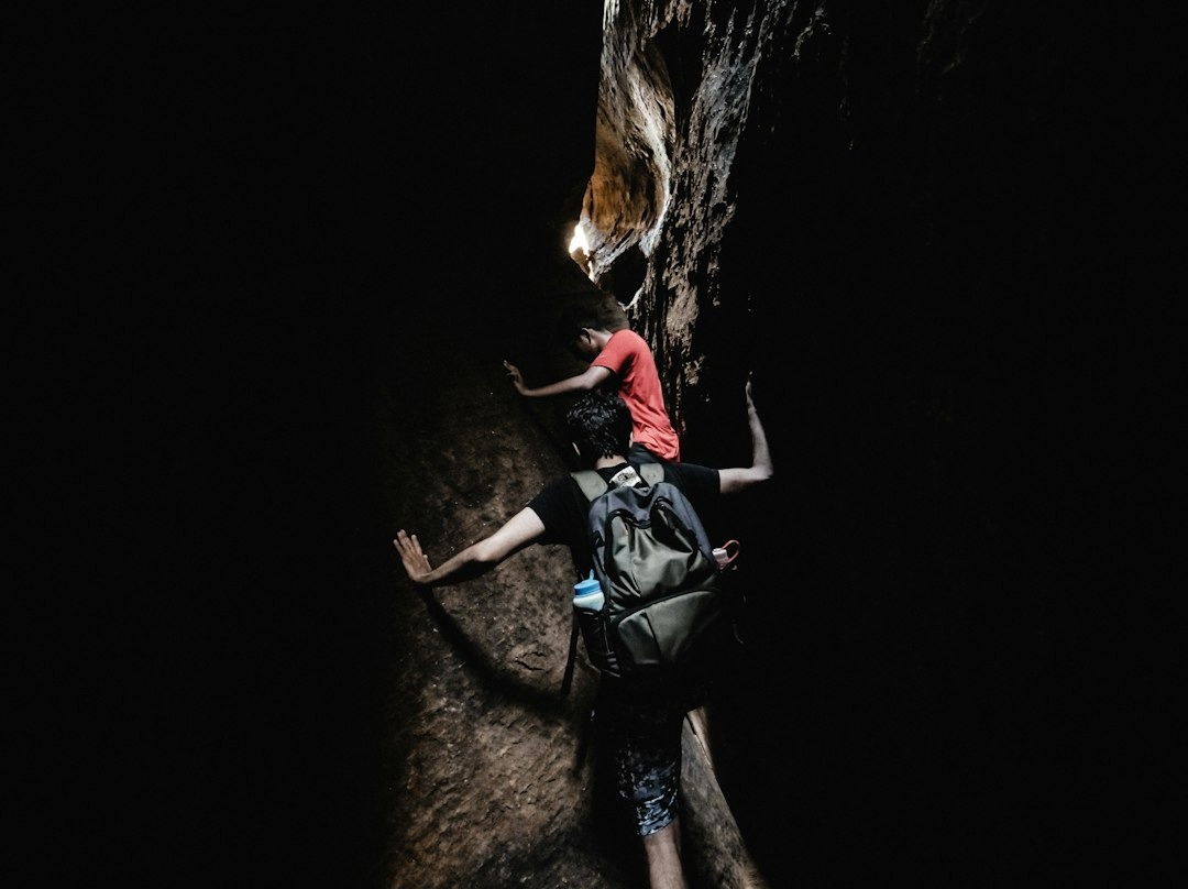 two boy's climbing between black and grey rocks during daytime