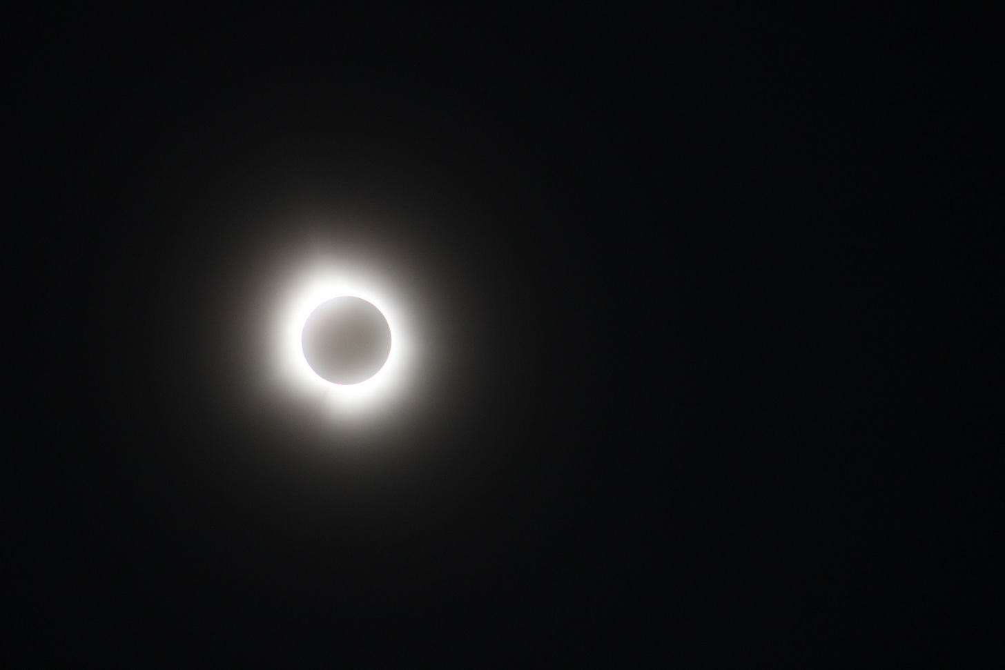 A view of a total solar eclipse.  The sky is black, the sun is radiating out from behind the moon.