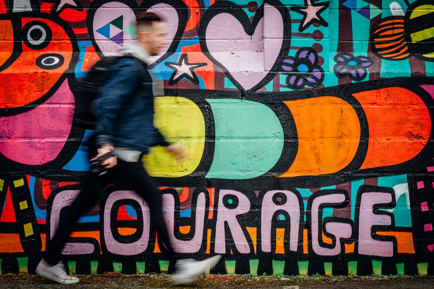 A colorful mural includes the word "courage" in a photograph that has a blurry man walking by