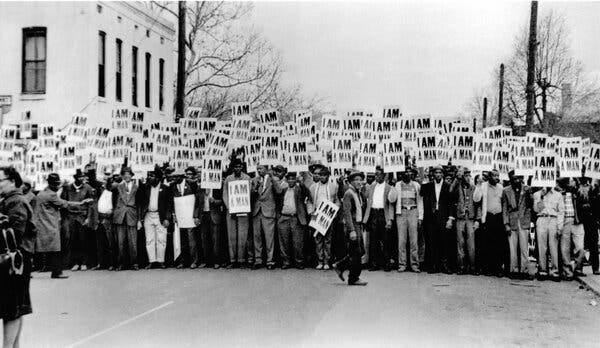 A large group of protesters stand in a row holding signs that say "I AM A MAN."