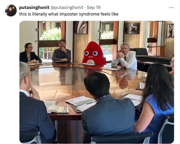 Tweet from @putasinghonit with text "this is literally what imposter syndrome feels like" a picture of a business meeting with someone dressed in a poop emoji costume.