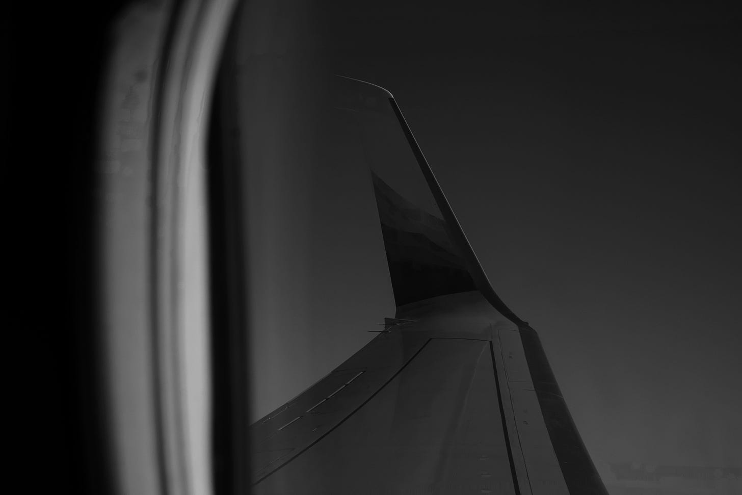 ala di un aereo forografata in bianco e nero attraverso un finestrino