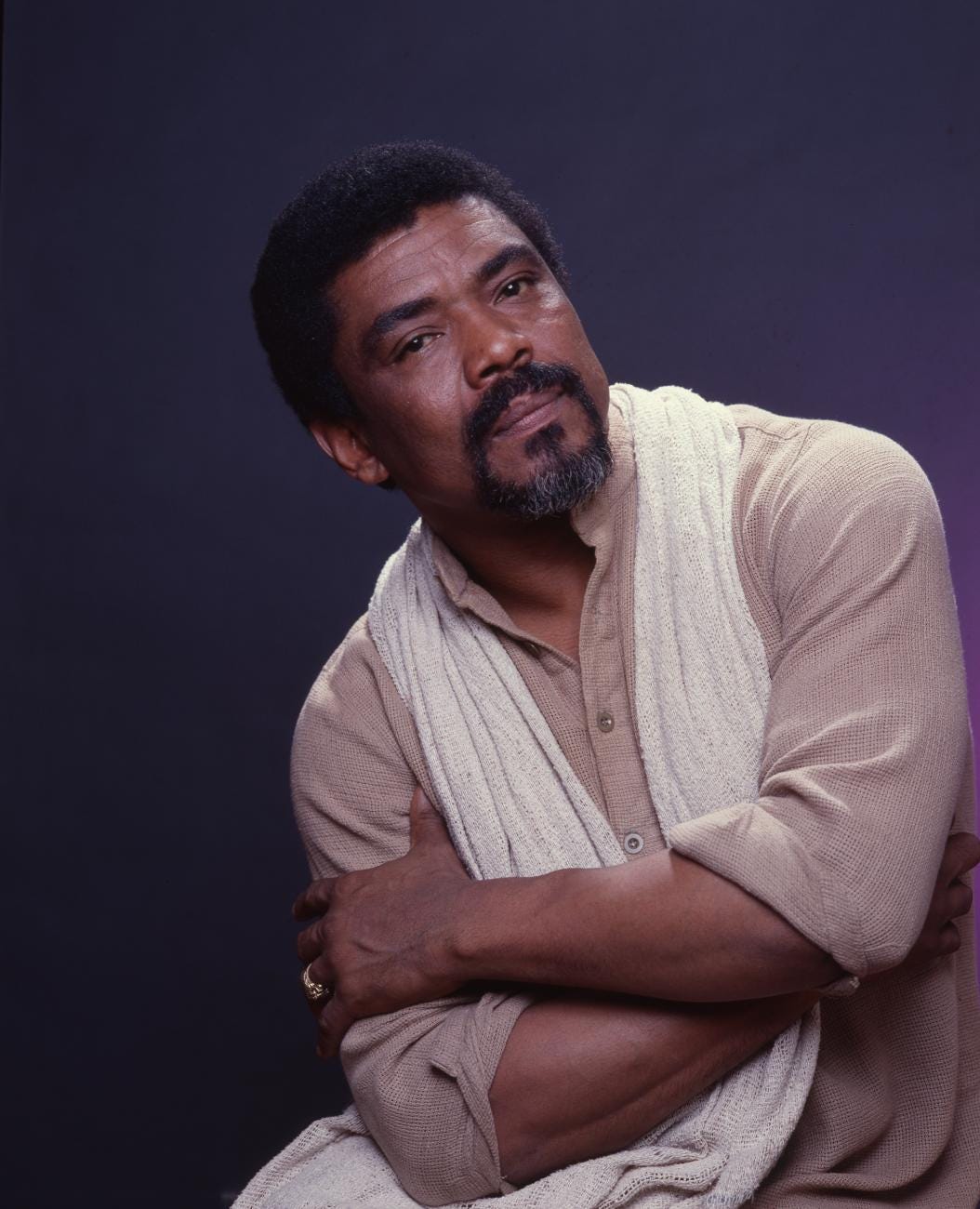 Portrait of Alvin Ailey wearing a sweater and scarf with his arms crossed in front of him. 