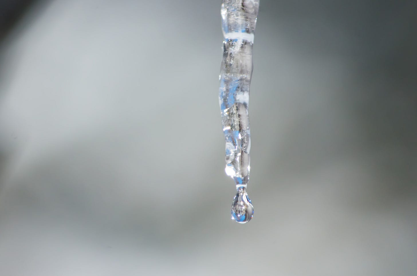 A crystal droplet is almost ready to fall from the tip of a melting icicle.