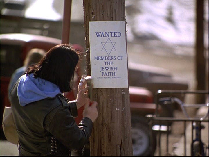 A young man in a leather jacket puts a flyer that reads "Wanted Members of the Jewish Faith" on a utility pole.