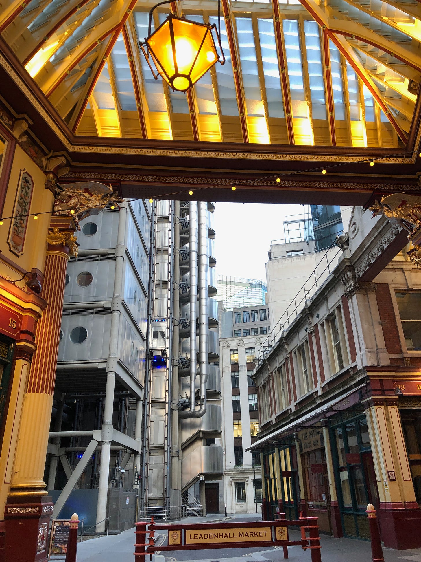 Glass-roofed market building, lamp above, combination of industrial and historic buildings visible through the opening. The sign in the foreground reads: "Leadenhall Market".