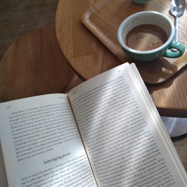 Birds eye view of a coffee table with a black coffee in a blue mug on a wooden table, and an open book with the subheading 'Sabotaging power'
