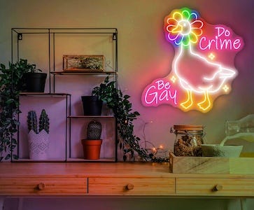 a wall with plants and a neon sign of a goose with flower petals around its head and the text Be Gay, Do Crime