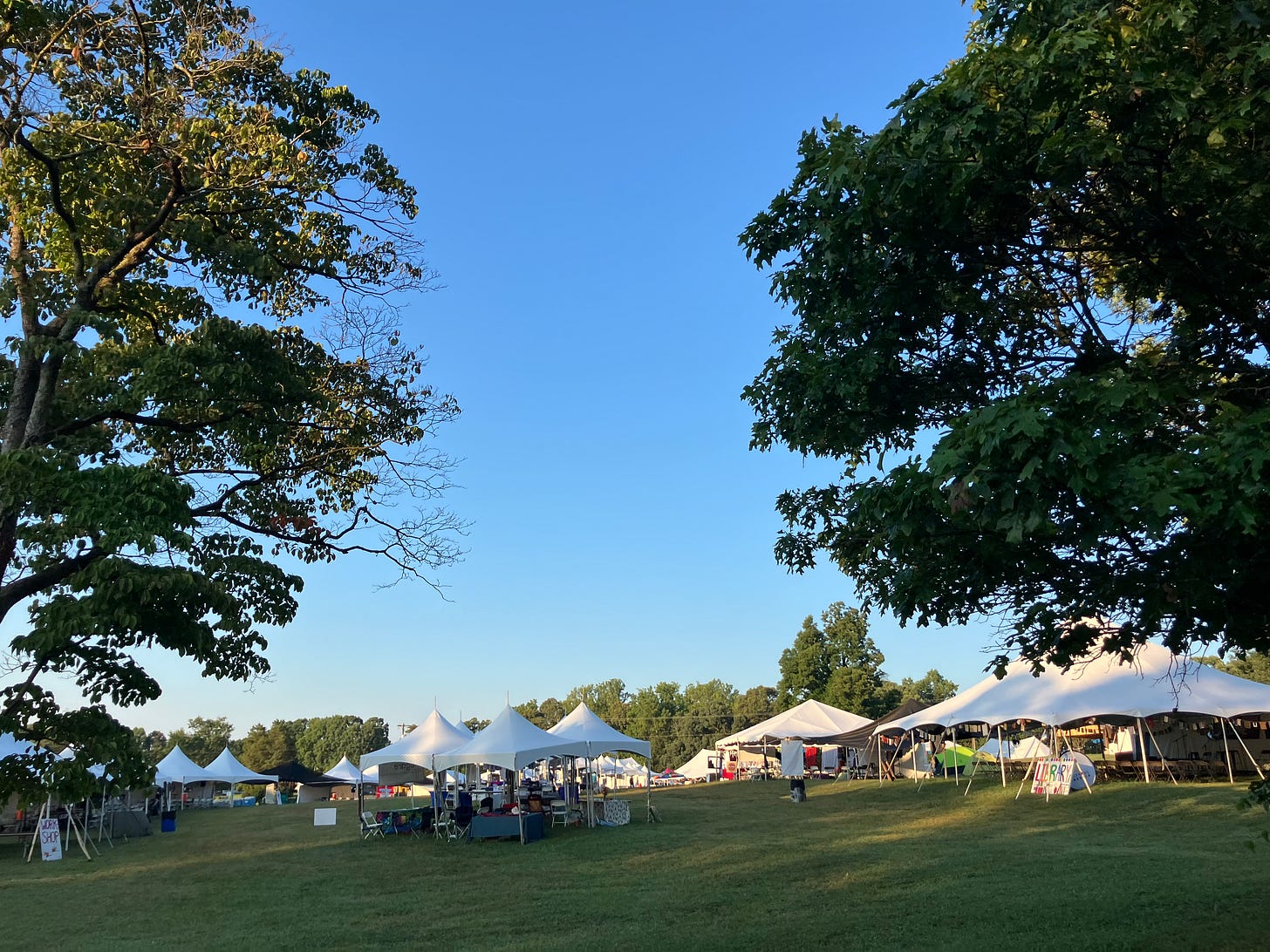 A photograph of even tents framed by trees under a blue sky
