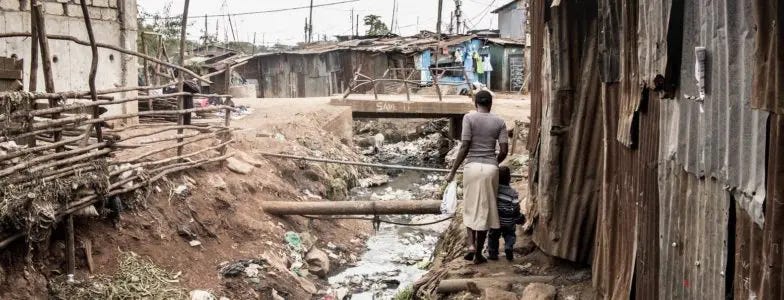 People walking along an open sewer in a slum in Africa