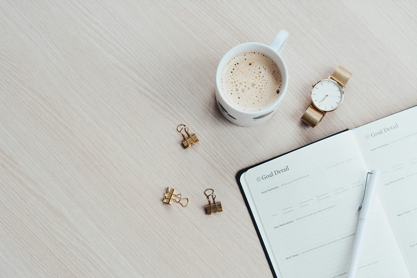 goals book, coffee cup with coffee, watch, and clips on a table