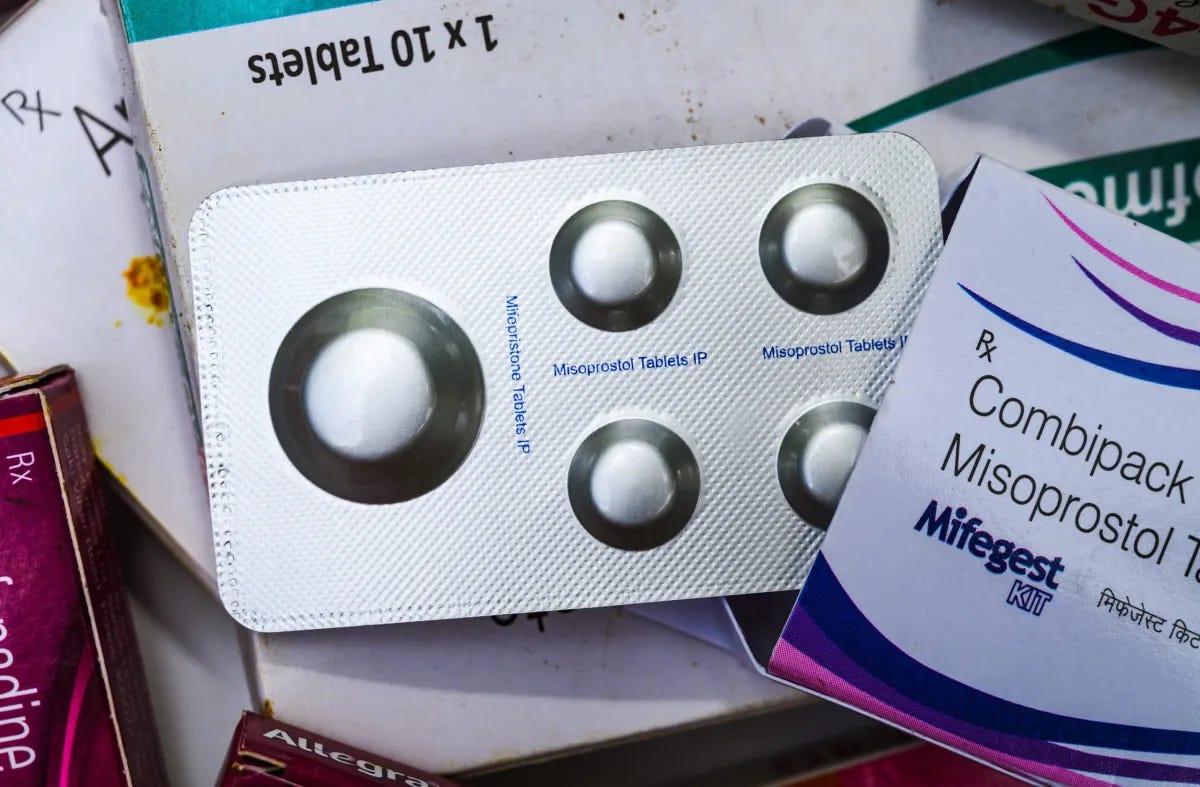 A photo of a foil pack of Mifepristone and Misoprostol pills, partially pulled out of the box they came in, marked “Mifegest Kit.”