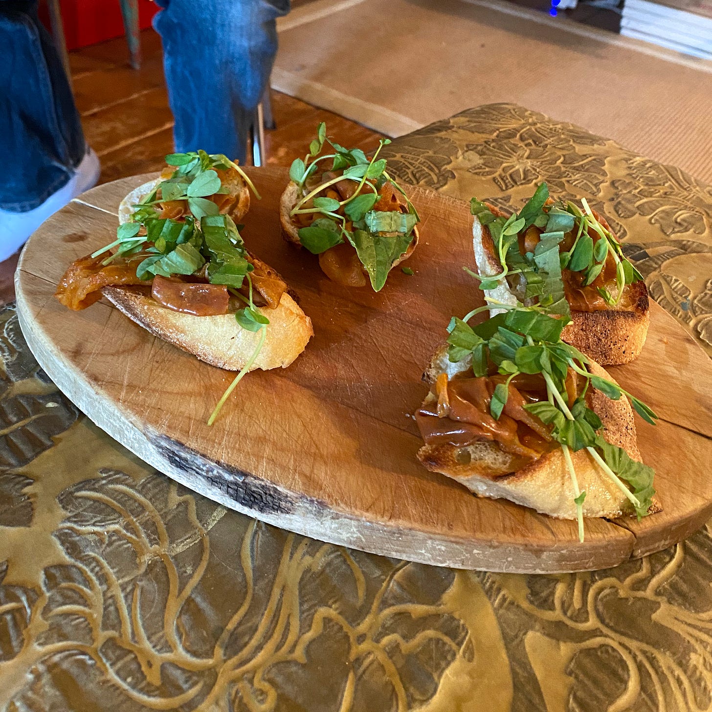 On a round bread board, slices of baguette with rice paper 'ham', pea shoots, and basil. 