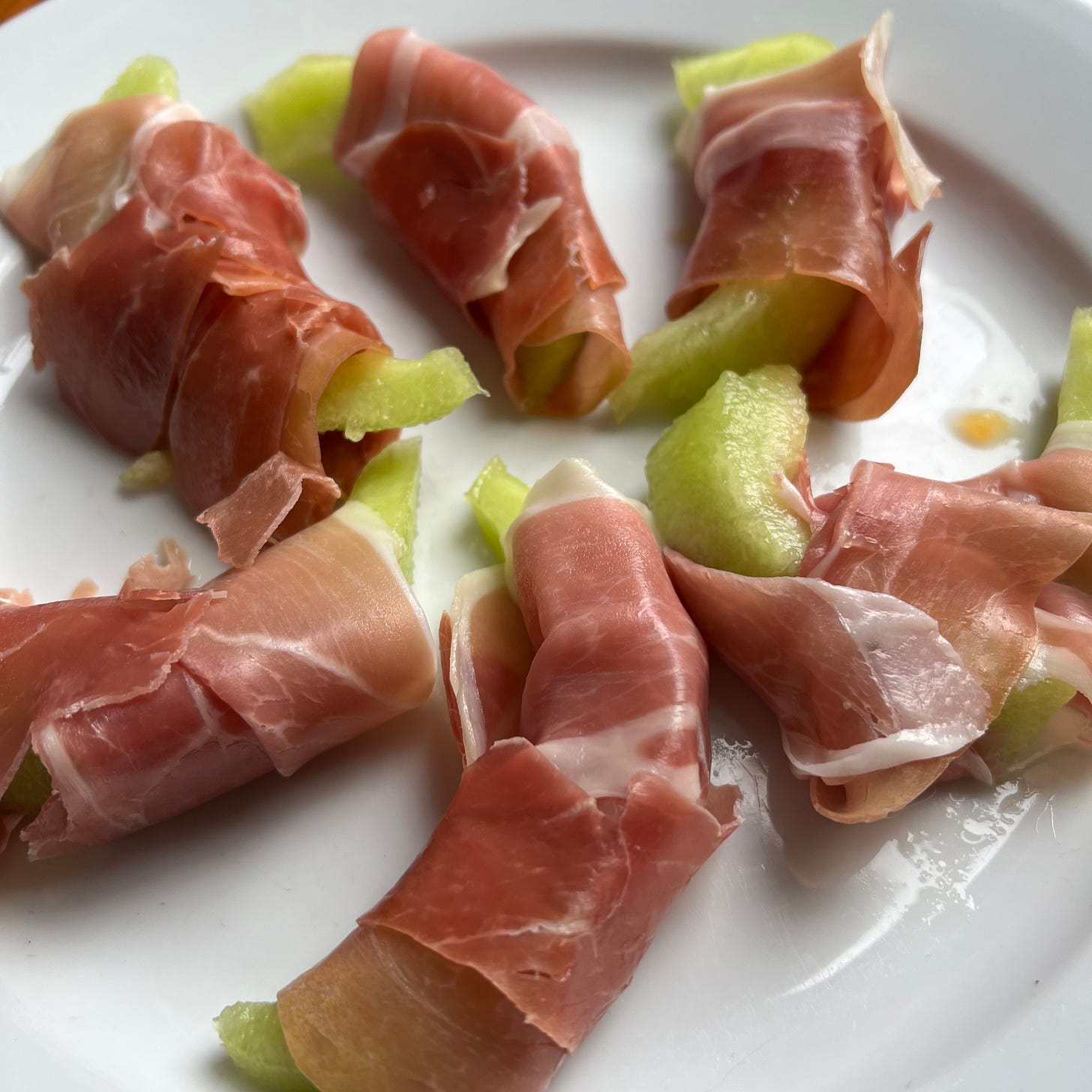 Pink Parma ham slices wrapped around slices of green honey dew melon on a white plate