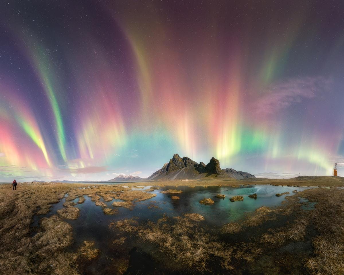 The image captures a panoramic view of Eystrahorn Mountain with dancing aurorae surrounding it.