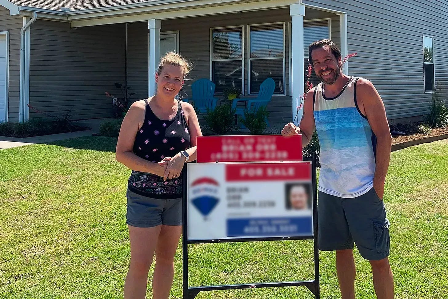 Donetta and James stand in front of the house for sale sign.