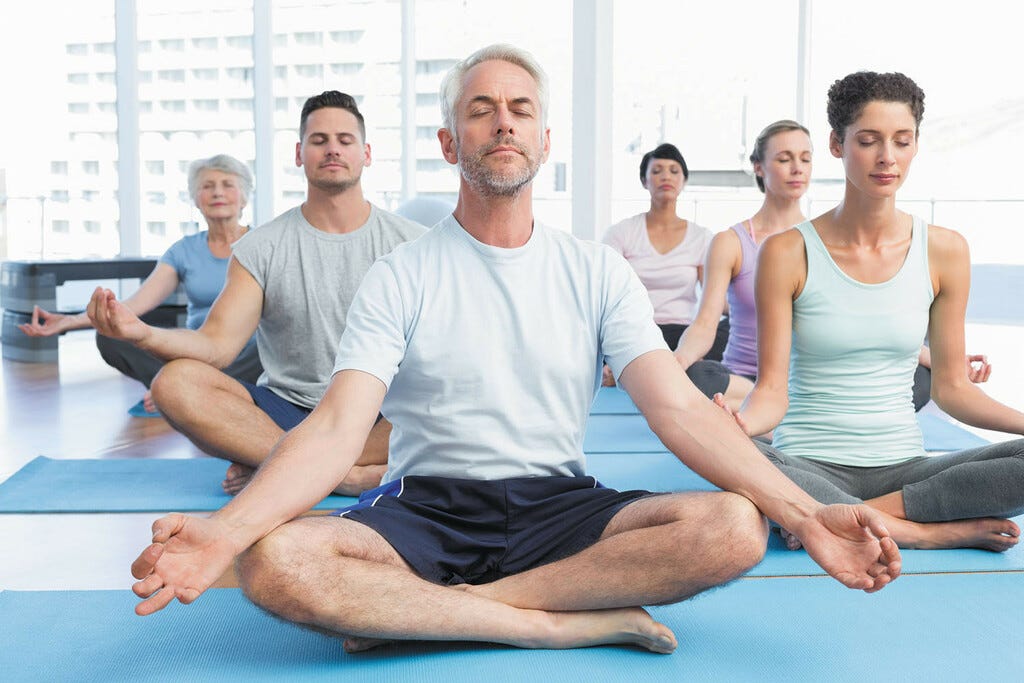 Six personnes font du yoga sur des tapis de gym à l'étage d'un immeuble couvert de baies vitrées.