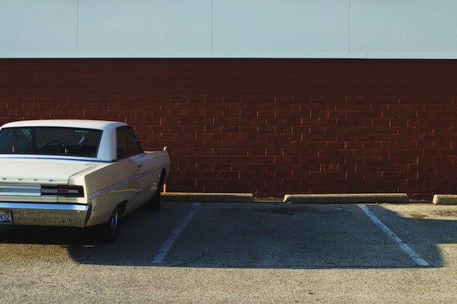 photo of a large old car in a parking lot with an empty space next to it