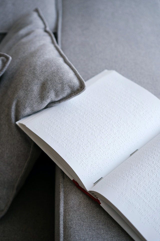 On a grey sofa, with a grey cushion, a white book filled with braille lies open