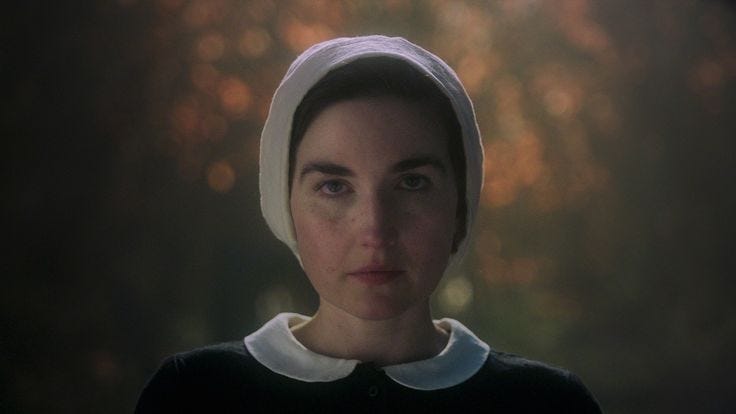 This may contain: a woman wearing a white bonnet and black dress in the dark with trees in the background