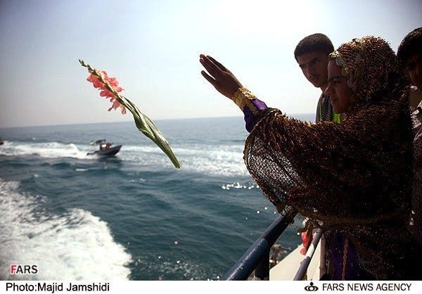 With patrol boats in the background, an Iranian woman tosses flowers into the ocean where Iran Air Flight 655 was shot down, as others look on. 