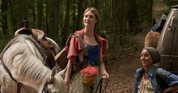 a screencap from Station Eleven, showing a white woman smiling and leading a horse