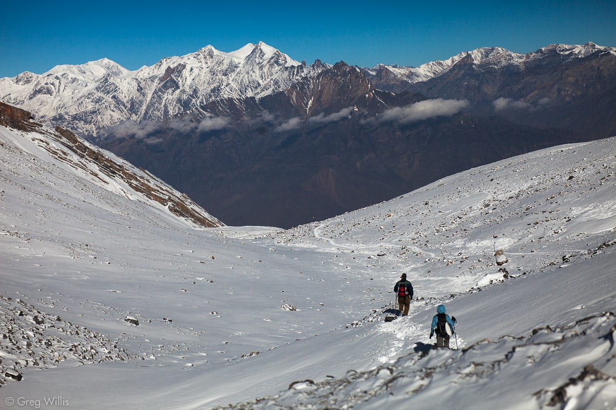 Hikers climbing a beautiful snow covered mountain, with sharp mountain peaks visible ahead of them