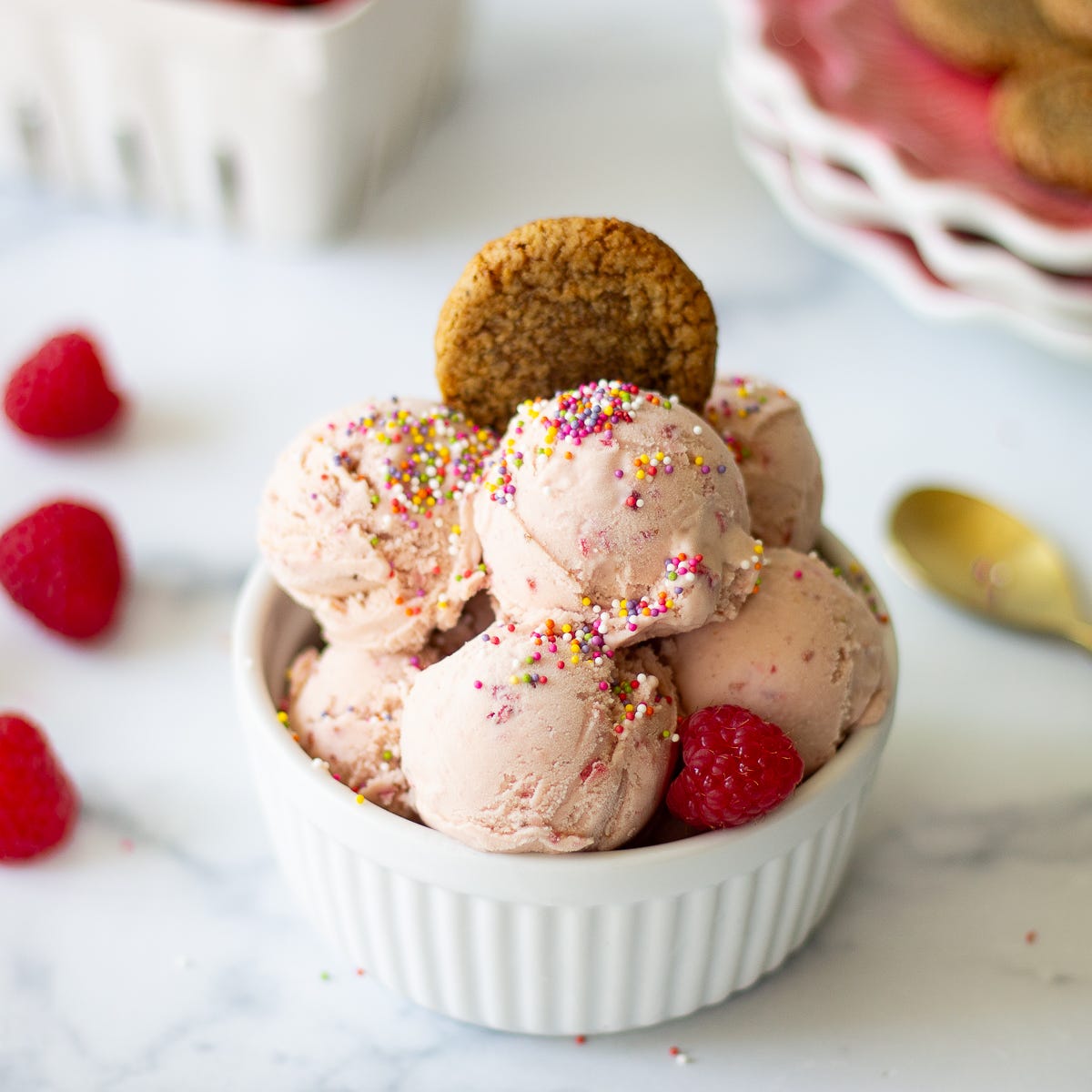 Several scoops of raspberry ice cream in a white ramekin with a cookie on top. 