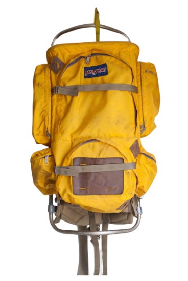 A vintage yellow jansport backpack on an aluminum frame