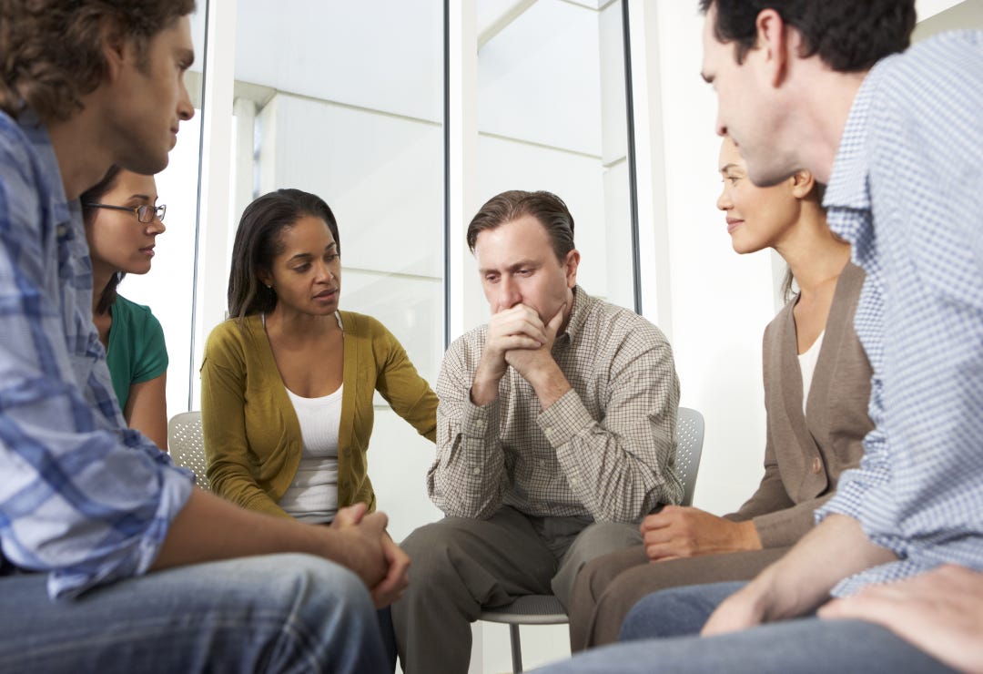 black woman consoles emotionally distraught white man in a support group of mostly white people