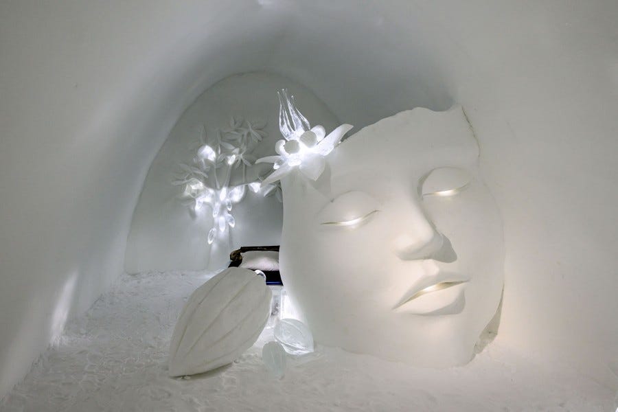 A snow-carved room is nearly filled by a snow sculpture of a person's face and some ornaments.