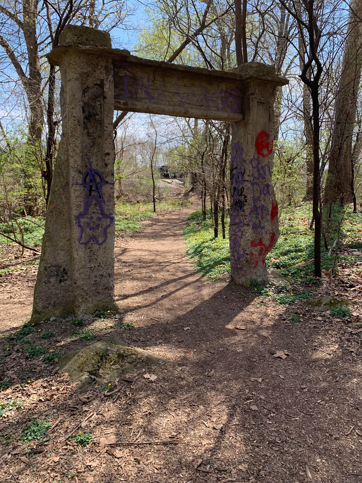 A weathered and graffitied stone archway in the middle of a wooded path