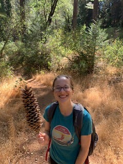 woman with glasses holding a pinecone larger than her head