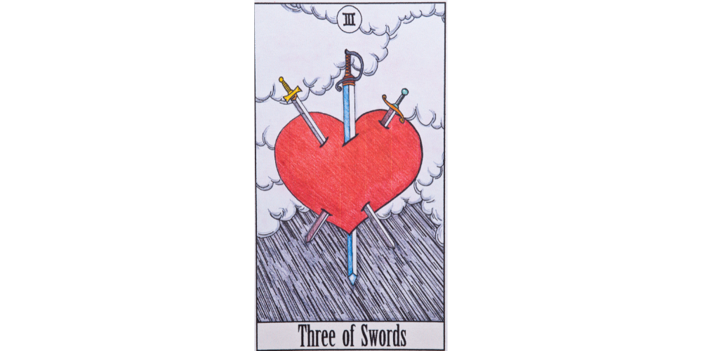 The three of swords tarot card from the Rider Waite Smith deck. Description follows in text.